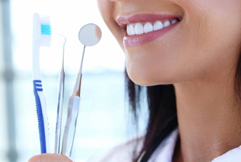 Smiling female dentist holding tool and toothbrush in her hands